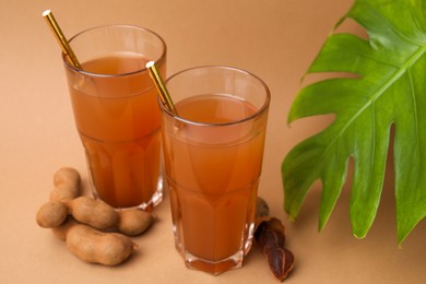 Photo of Tamarind juice, fresh fruits and green leaf on pale brown background, closeup