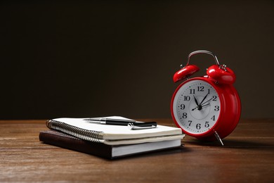 Photo of Alarm clock and office stationery on wooden table against dark background, space for text. Time management