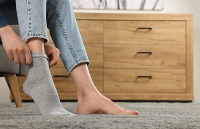 Photo of Woman putting on grey socks at home, closeup. Space for text