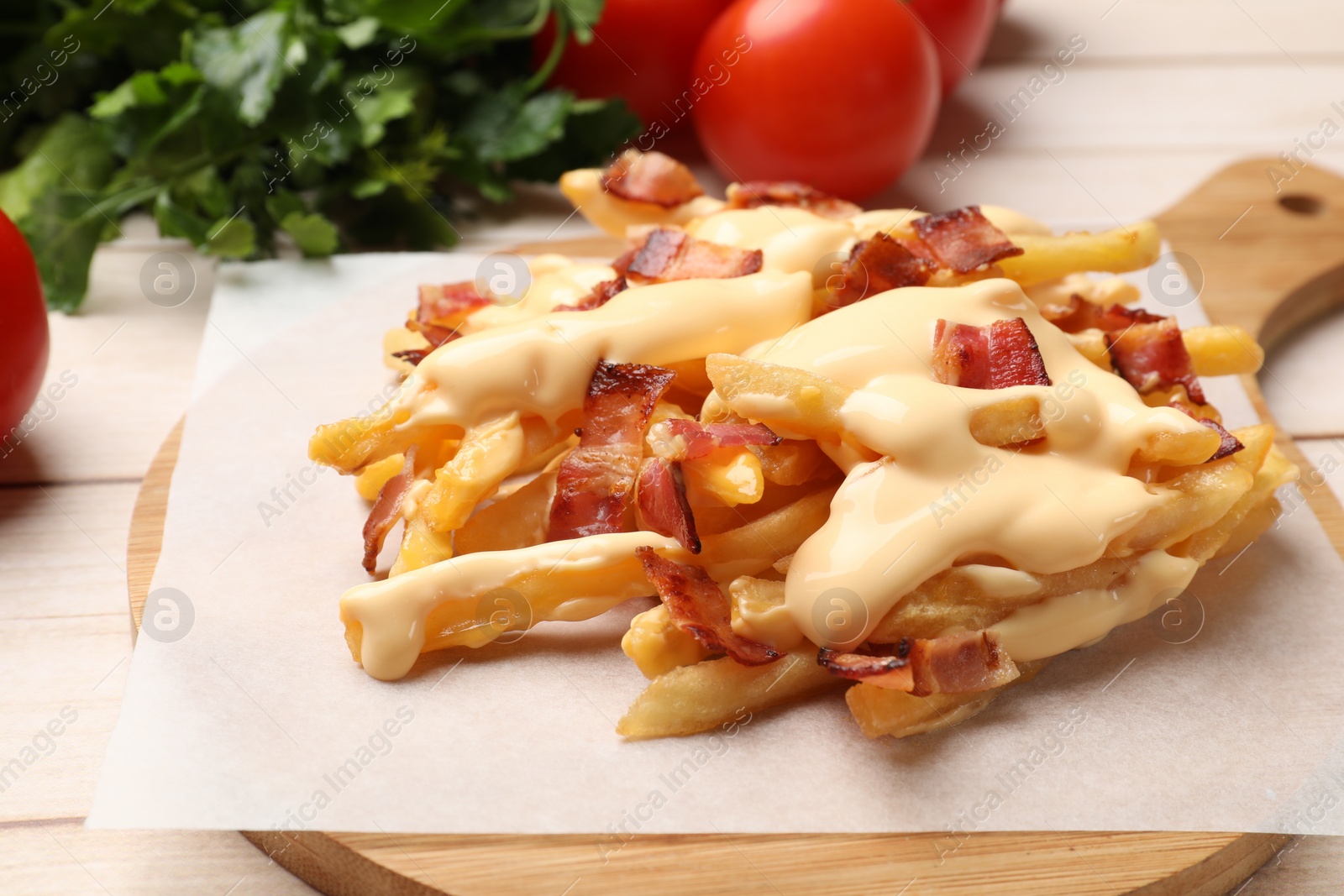 Photo of Delicious French fries with bacon, cheese sauce, tomatoes and herbs on wooden table, closeup