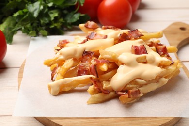 Delicious French fries with bacon, cheese sauce, tomatoes and herbs on wooden table, closeup