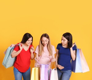 Happy pregnant women with shopping bags on orange background