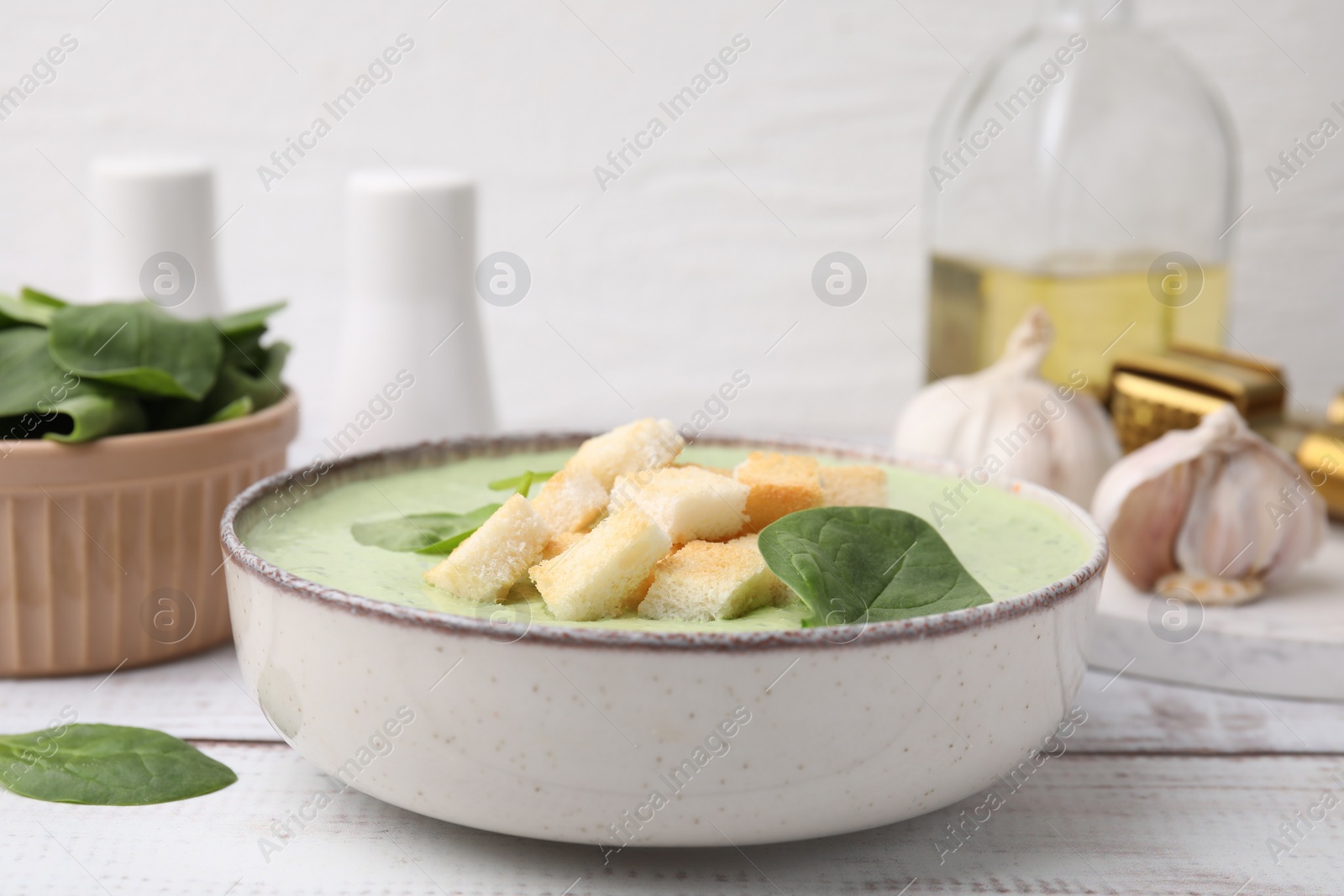 Photo of Delicious spinach cream soup with leaves and croutons in bowl on white wooden table