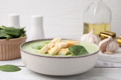 Delicious spinach cream soup with leaves and croutons in bowl on white wooden table