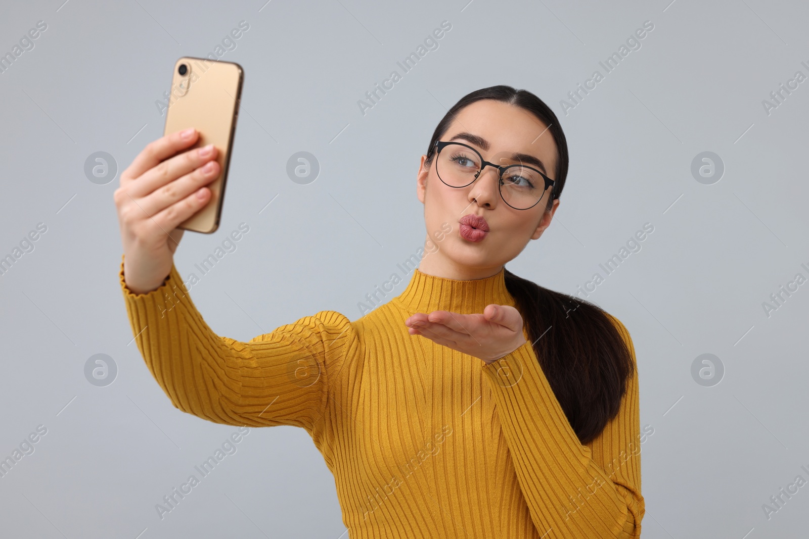 Photo of Young woman taking selfie with smartphone and blowing kiss on grey background