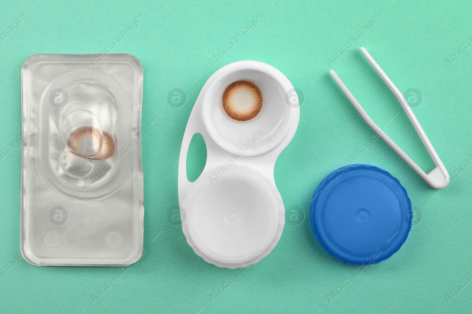 Photo of Case with color contact lenses, tweezers and package on turquoise background, flat lay