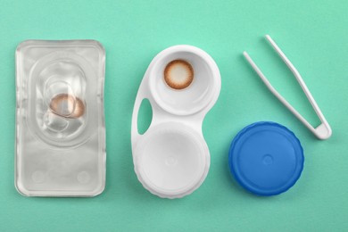 Photo of Case with color contact lenses, tweezers and package on turquoise background, flat lay
