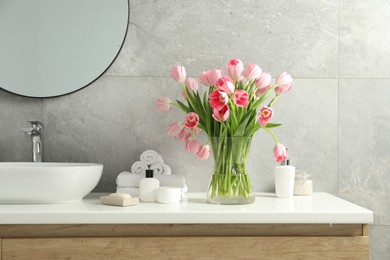 Photo of Vase with beautiful pink tulips and toiletries near sink in bathroom