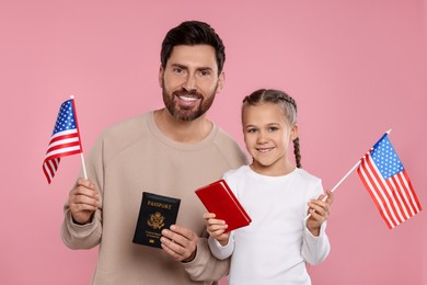 Photo of Immigration. Happy man with his daughter holding passports and American flags on pink background