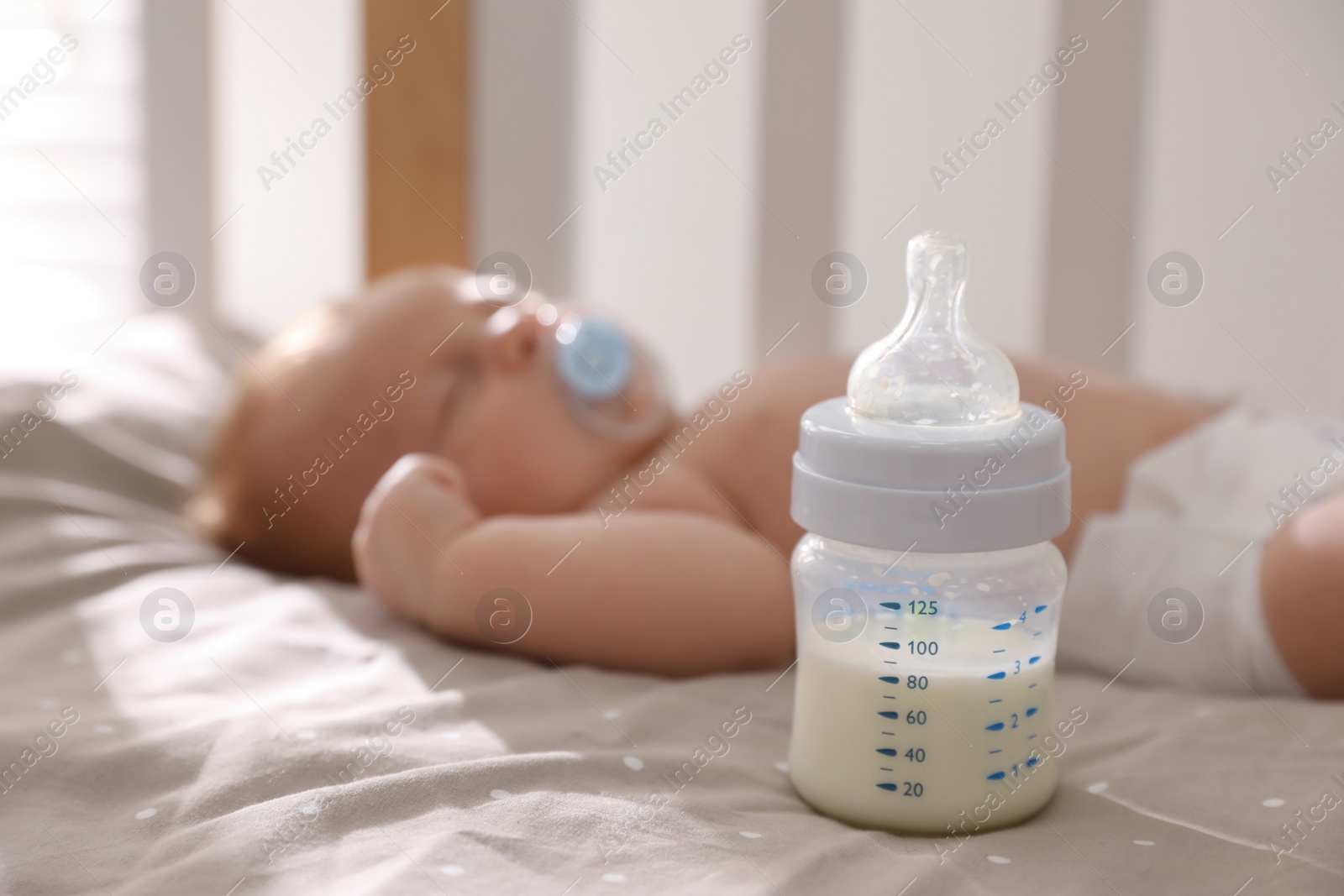 Photo of Healthy baby sleeping in cot, focus on bottle with milk