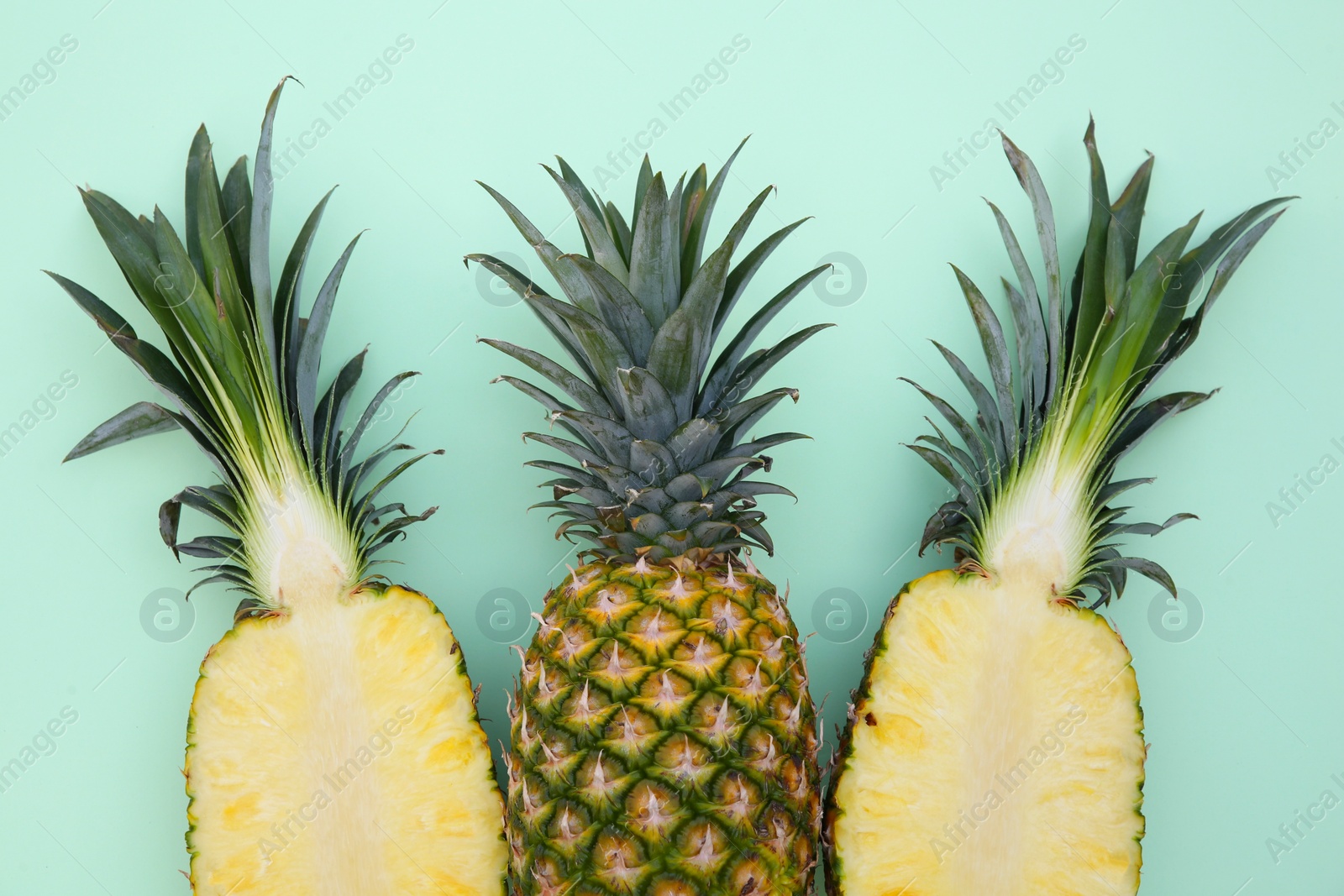 Photo of Whole and cut ripe pineapples on light green background, flat lay