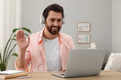 Man in headphones greeting someone during video chat via laptop at home