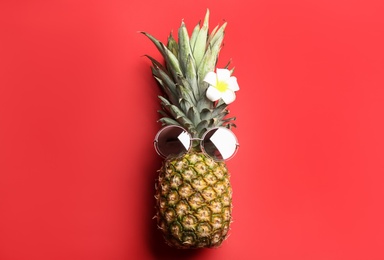 Pineapple with sunglasses and plumeria flower on red background, top view. Creative concept