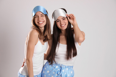 Photo of Beautiful women wearing sleeping masks on light grey background. Bedtime