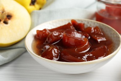 Photo of Tasty homemade quince jam in bowl and fruits on white wooden table, closeup