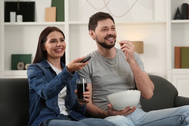 Photo of Happy couple watching show at home. Woman changing TV channels with remote control