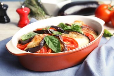 Baked eggplant with tomatoes, cheese and basil in dishware on table, closeup