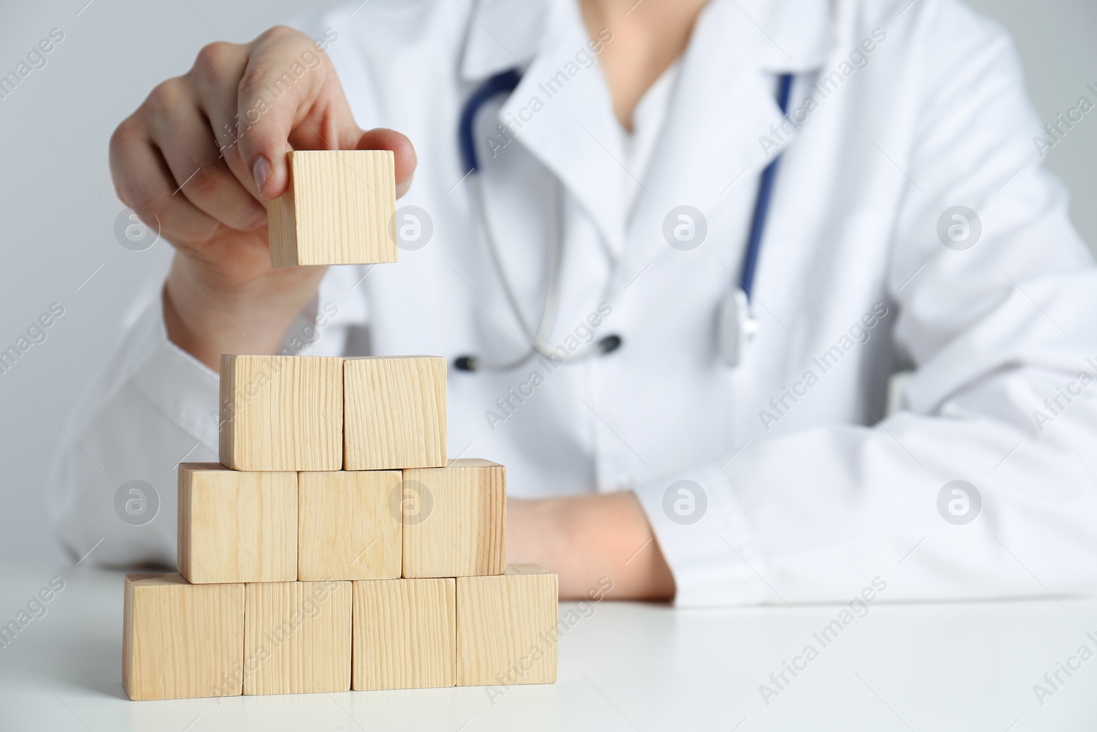 Photo of Doctor building pyramid of blank wooden cubes on white table against light background, closeup. Space for text