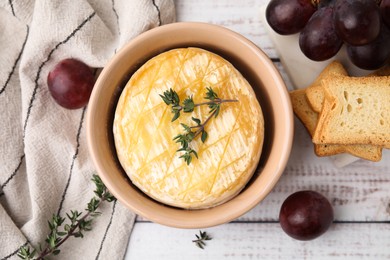 Photo of Tasty baked camembert in bowl, grapes, croutons and thyme on wooden table, flat lay