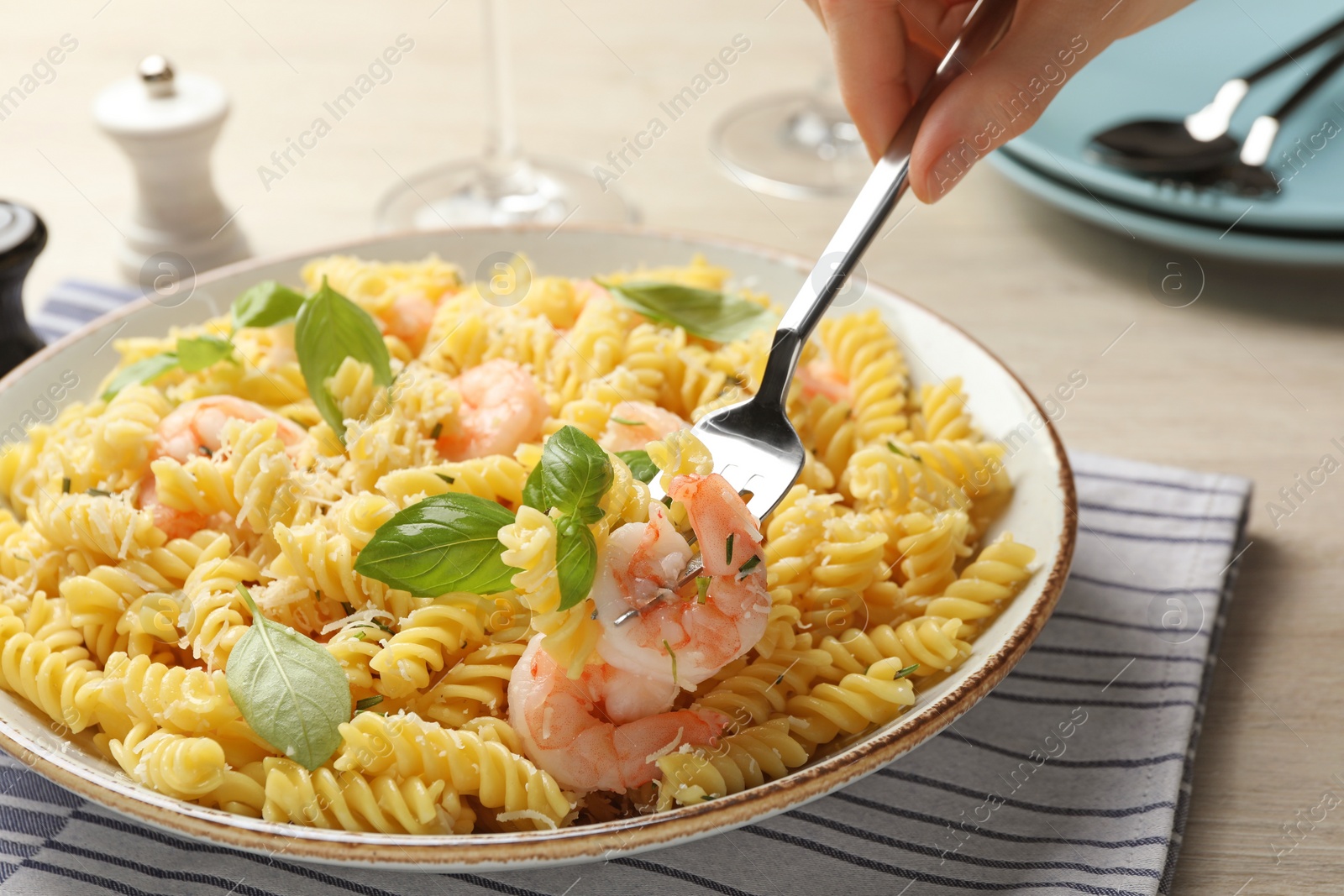 Photo of Woman eating delicious pasta with shrimps, basil and parmesan cheese at table, closeup