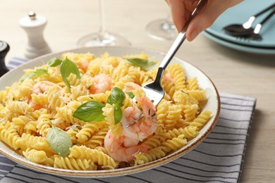 Woman eating delicious pasta with shrimps, basil and parmesan cheese at table, closeup