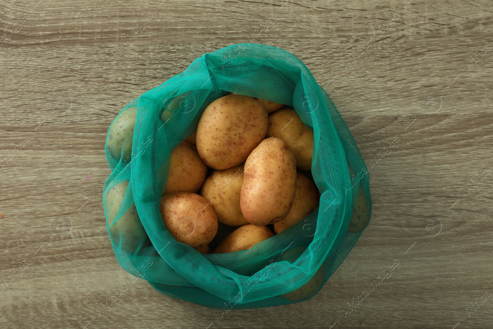 Photo of Net bag with potatoes on wooden table, top view