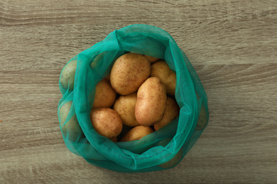 Photo of Net bag with potatoes on wooden table, top view