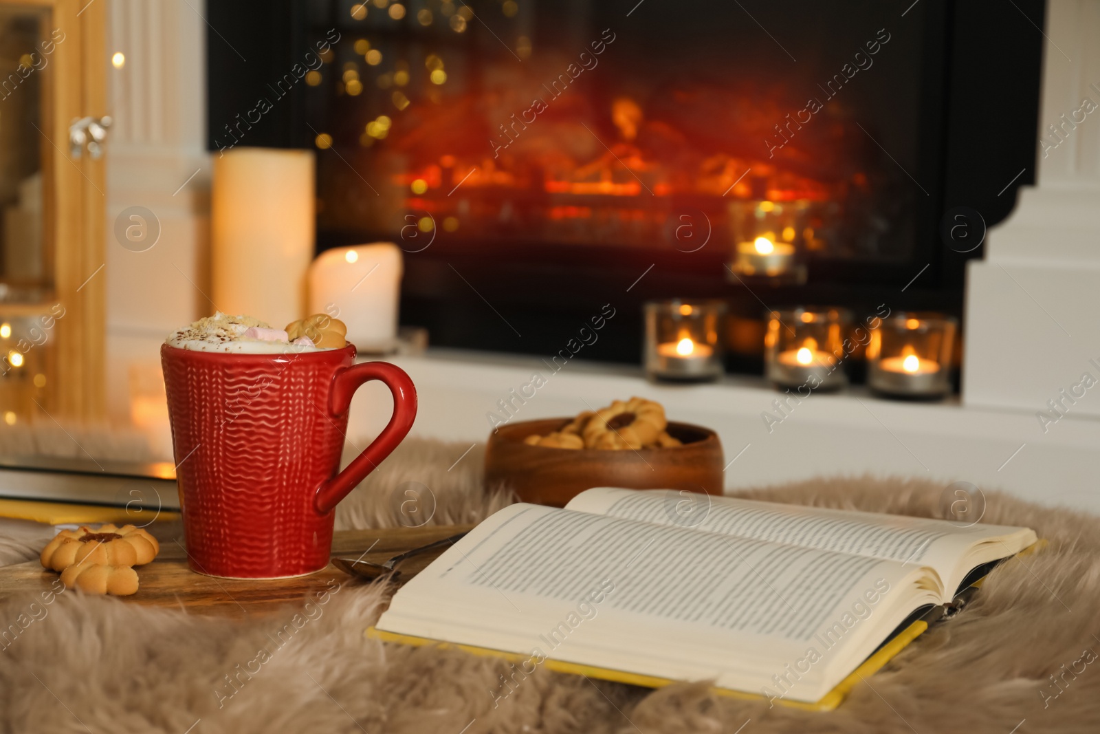 Photo of Cup of cocoa, book and cookies near fireplace indoors