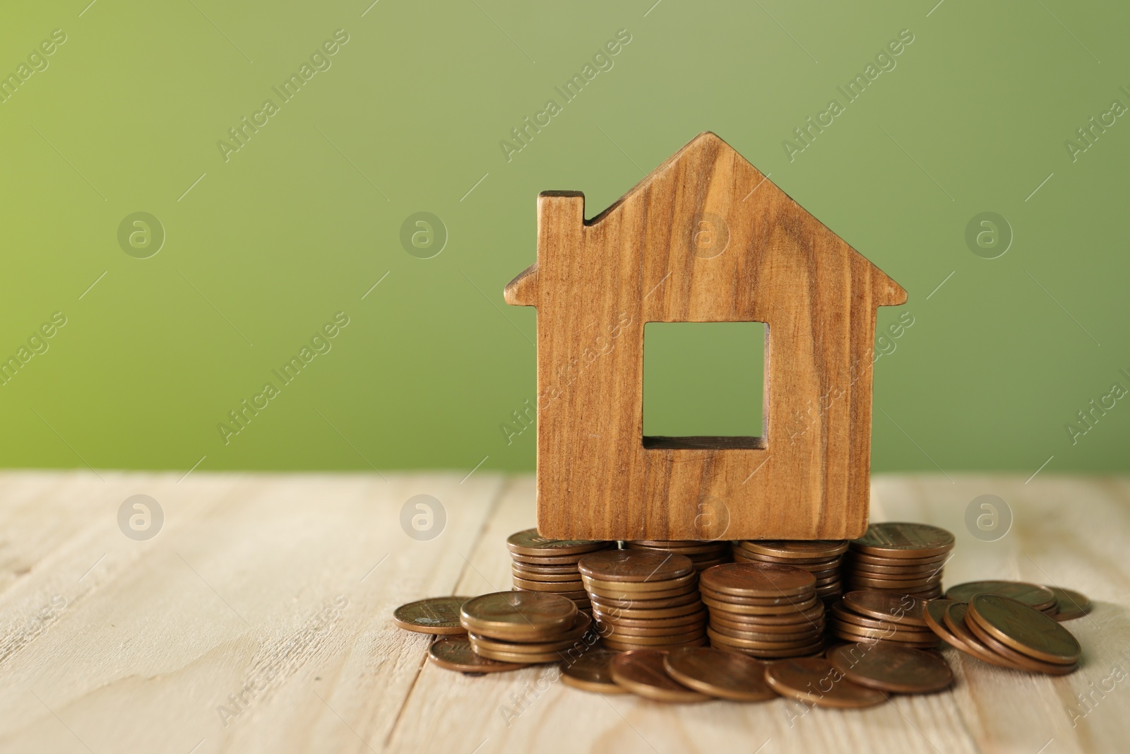 Photo of House model and coins on wooden table against green background, space for text