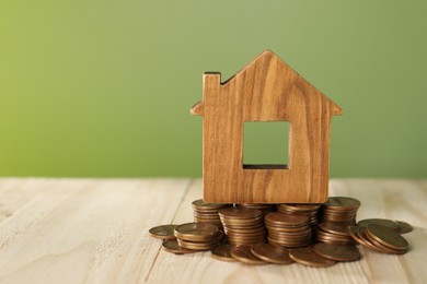 Photo of House model and coins on wooden table against green background, space for text