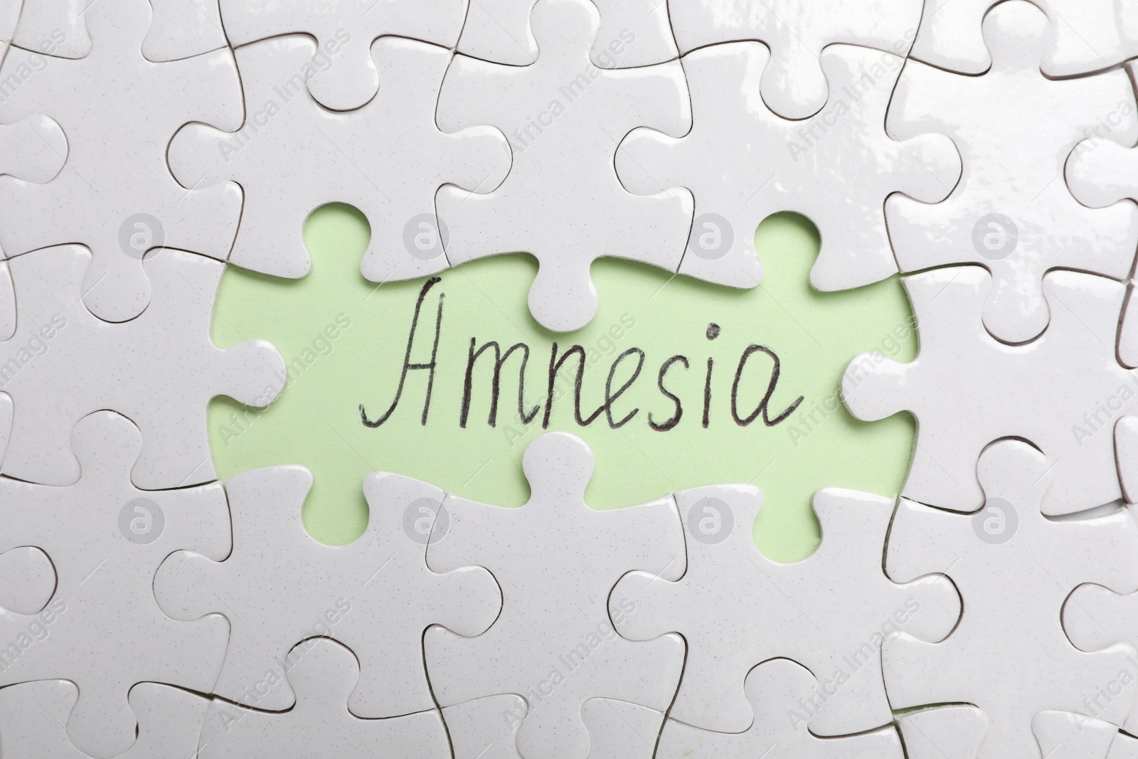 Photo of White puzzle pieces and word Amnesia written on light green background, flat lay