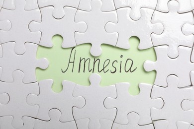 White puzzle pieces and word Amnesia written on light green background, flat lay