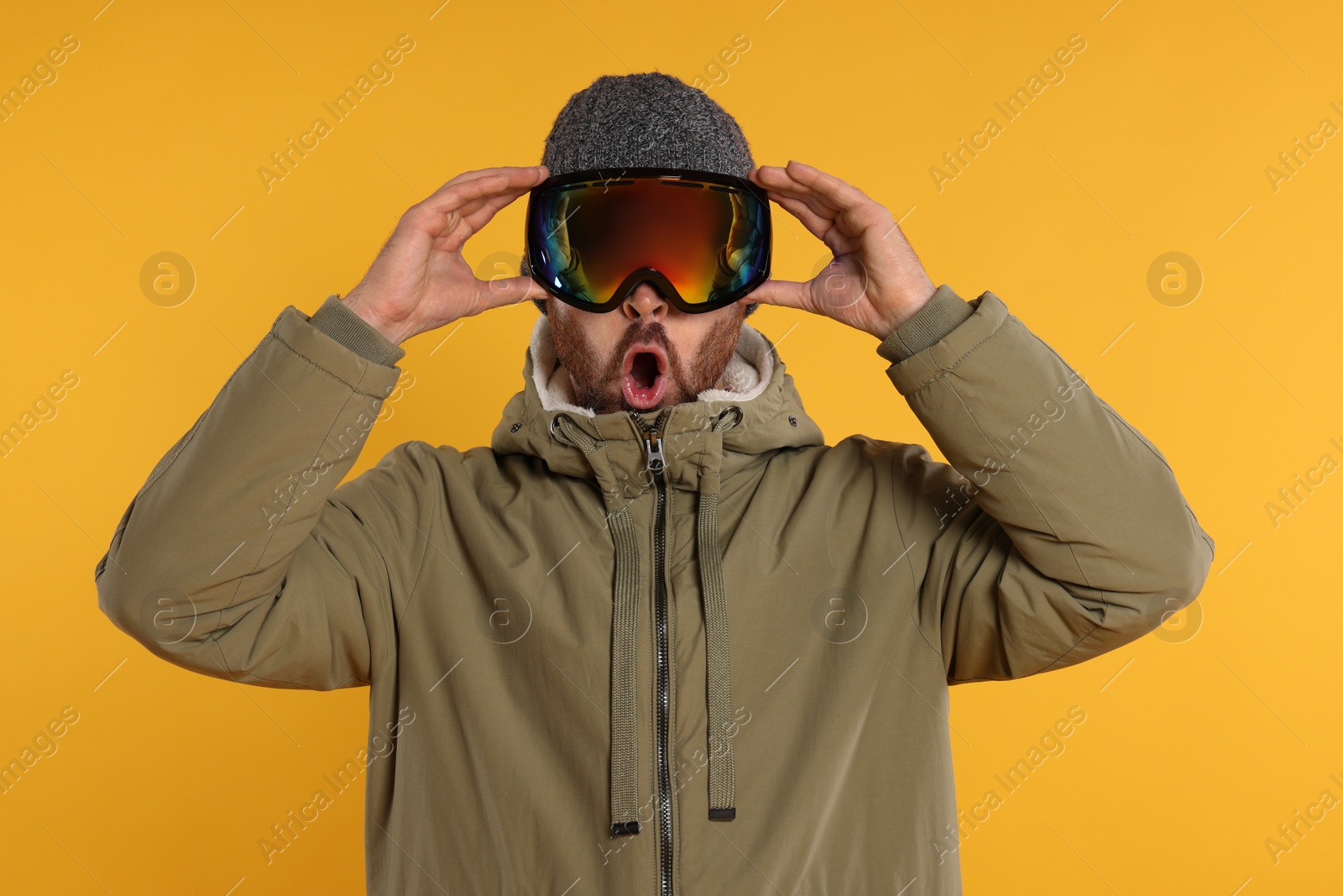 Photo of Winter sports. Emotional man in ski suit and goggles on orange background