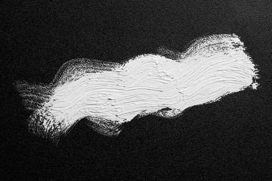 Photo of Strokes of white oil paint on black canvas, top view