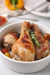 Photo of Delicious roasted chicken drumsticks with rosemary and tomatoes in bowl on white table, closeup