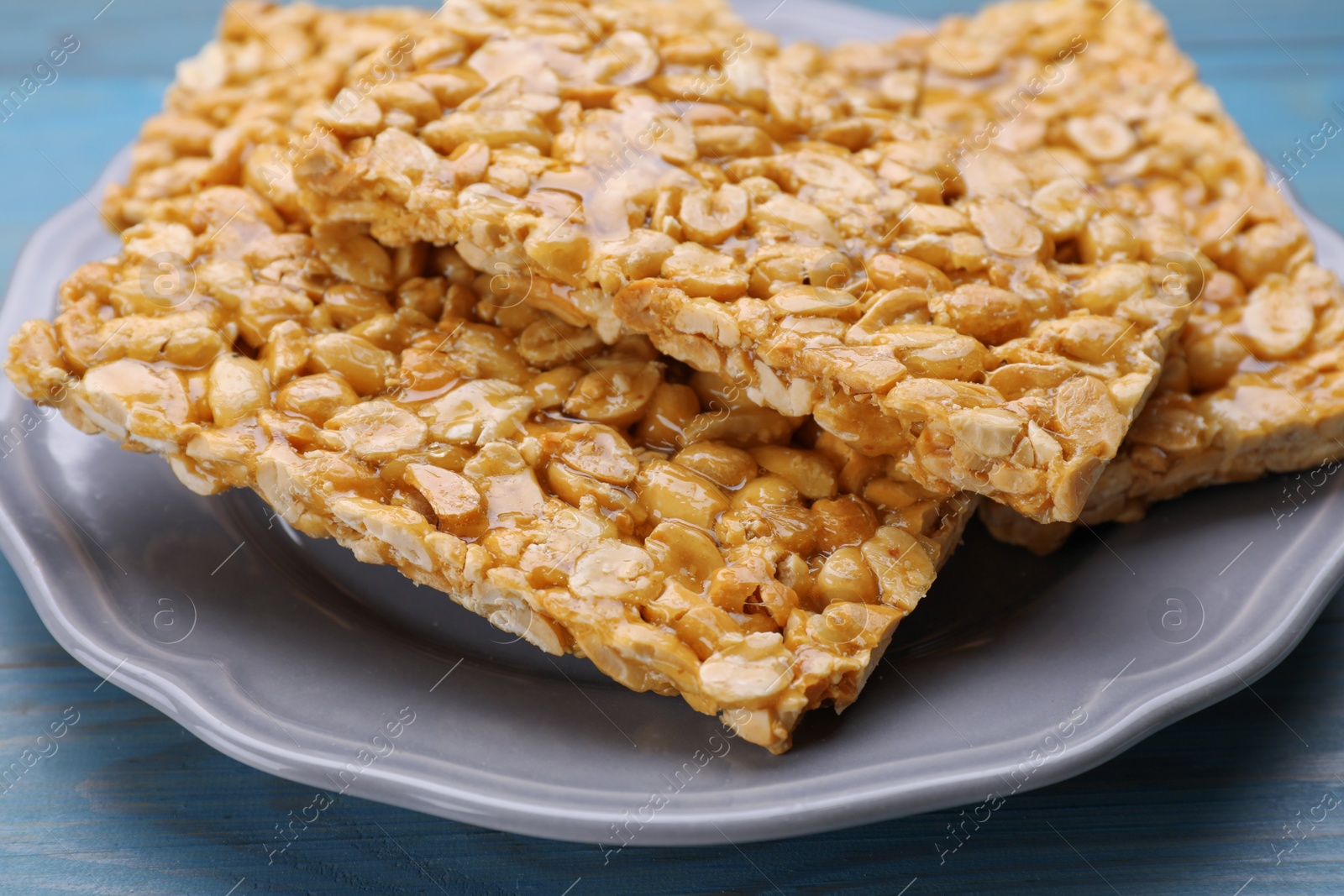 Photo of Delicious peanut bars (kozinaki) on light blue wooden table, closeup