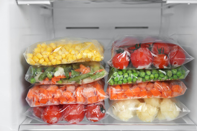 Plastic bags with different frozen vegetables in refrigerator