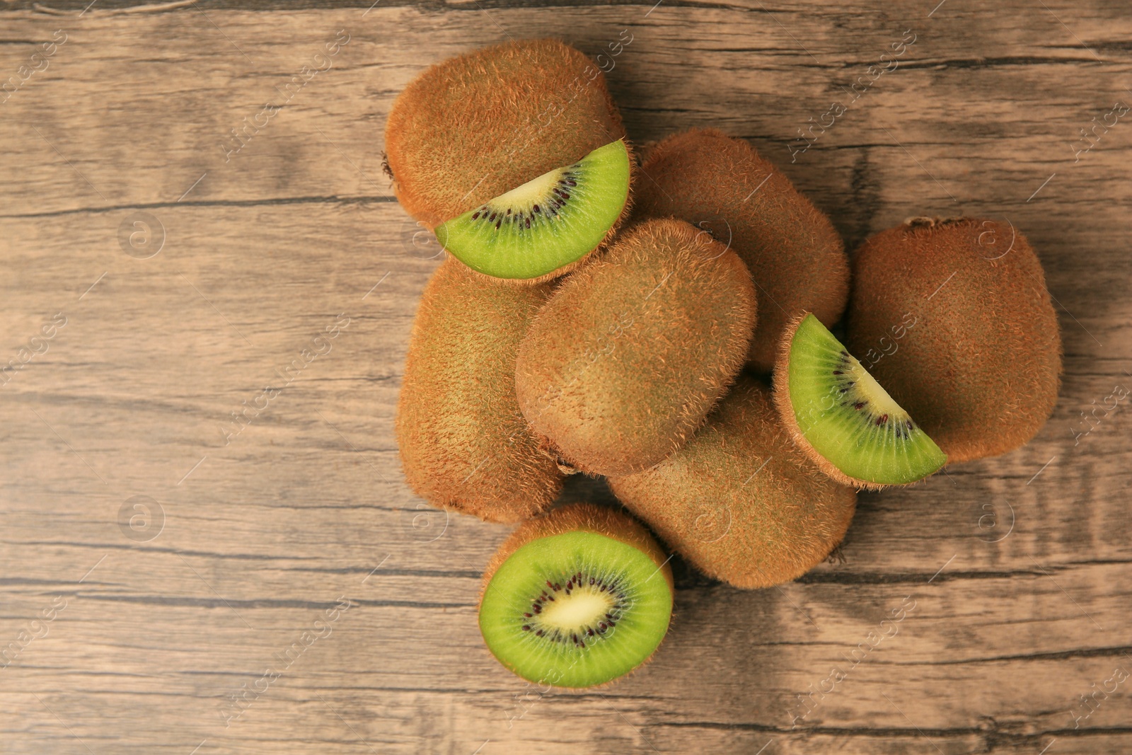 Photo of Heap of whole and cut fresh kiwis on wooden table, flat lay. Space for text