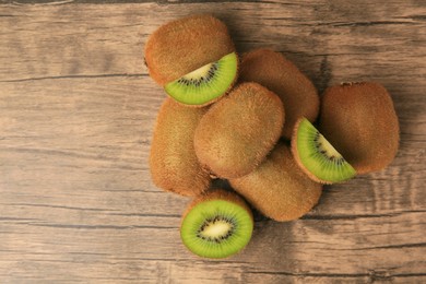 Photo of Heap of whole and cut fresh kiwis on wooden table, flat lay. Space for text