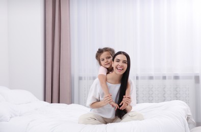 Photo of Happy woman and her daughter spending time together on bed at home, space for text. Mother's day celebration