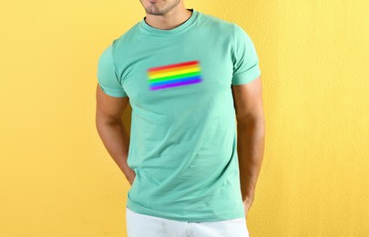 Image of Young man wearing turquoise t-shirt with image of LGBT pride flag on yellow background