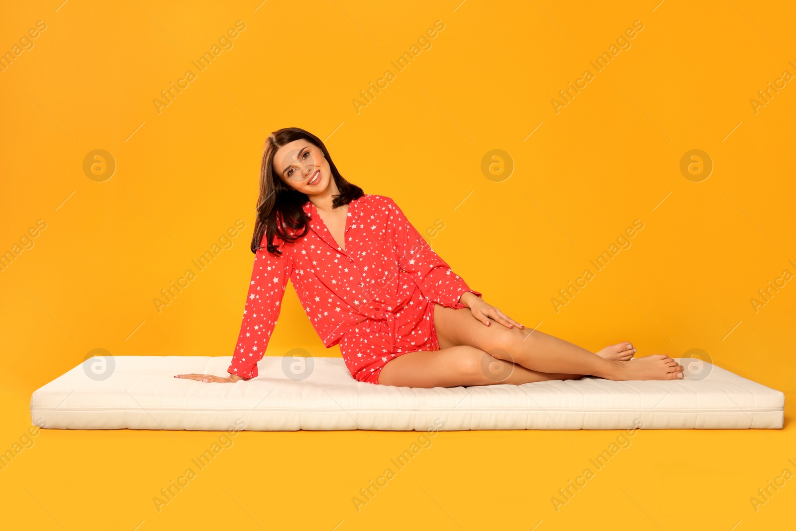 Photo of Young woman sitting on soft mattress against orange background