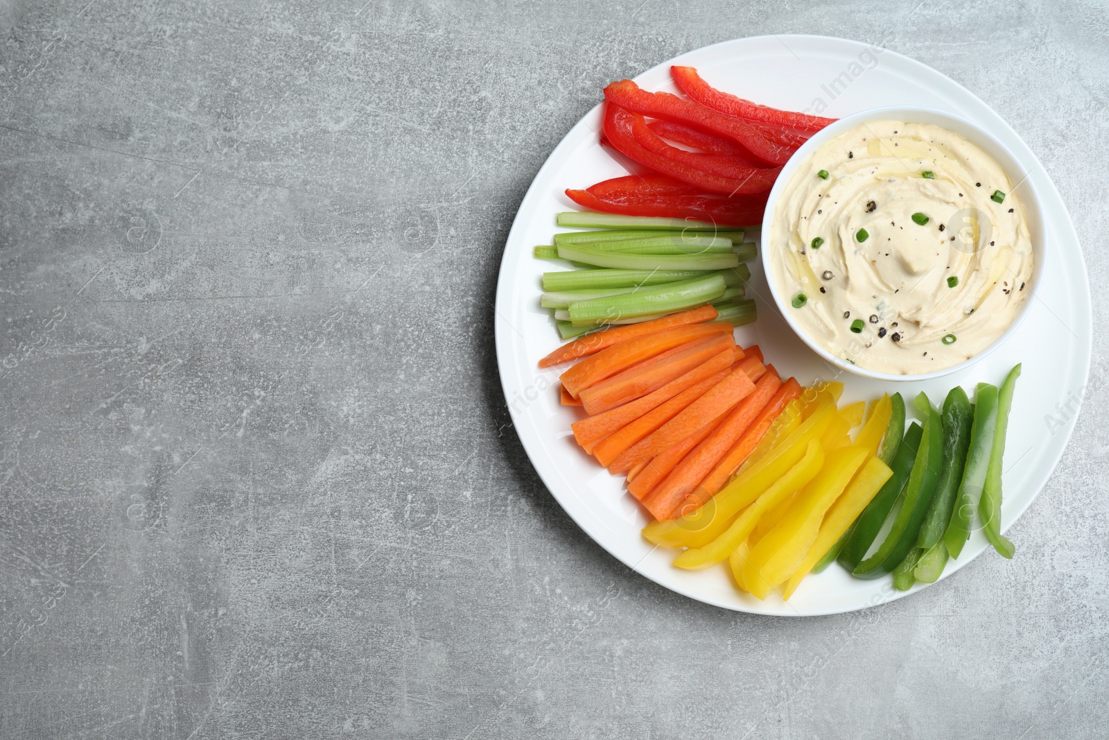 Photo of Fresh raw vegetable sticks and sauce on grey table, top view. Space for text