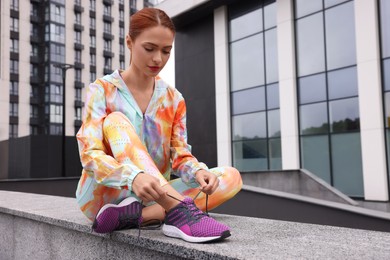 Photo of Woman sitting on parapet and tying shoelace of sneakers on street, space for text