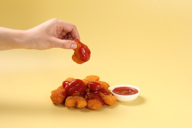Photo of Woman holding delicious chicken nugget with ketchup on pale yellow background, closeup