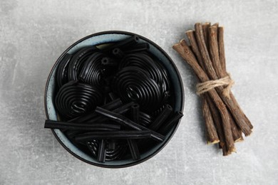 Photo of Tasty black candies and dried sticks of liquorice root on grey table, flat lay