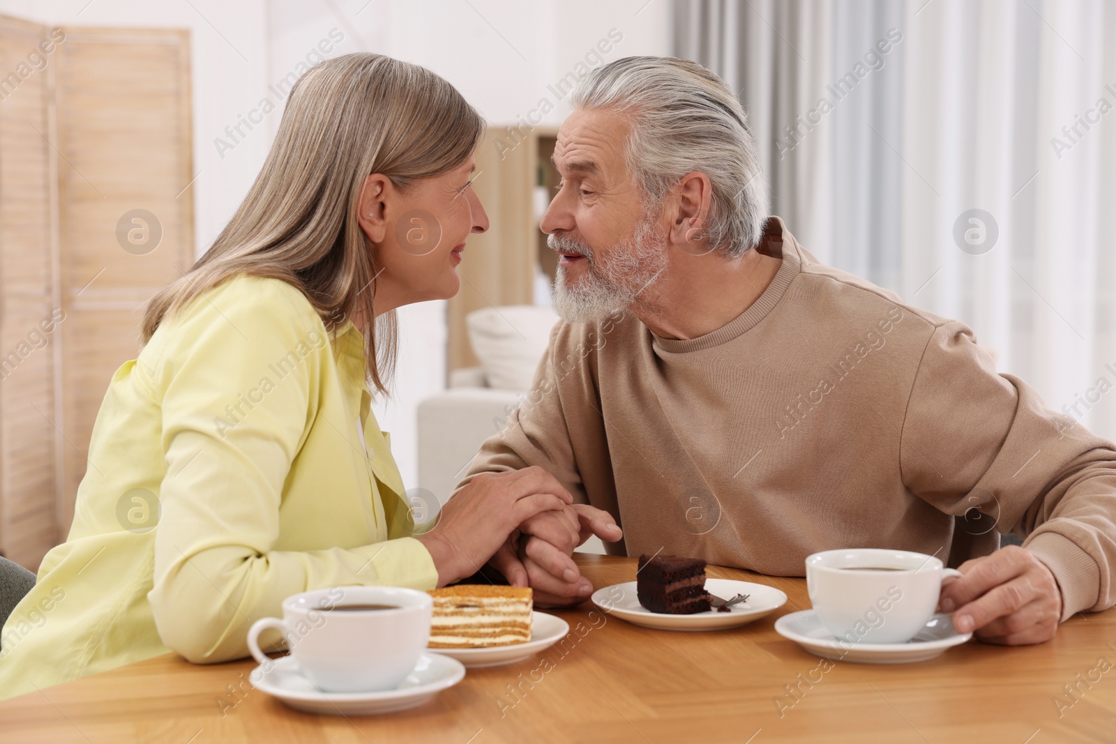 Photo of Affectionate senior couple having breakfast at wooden table in room