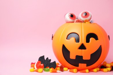Photo of Halloween trick or treat bucket with different sweets on pink background, space for text