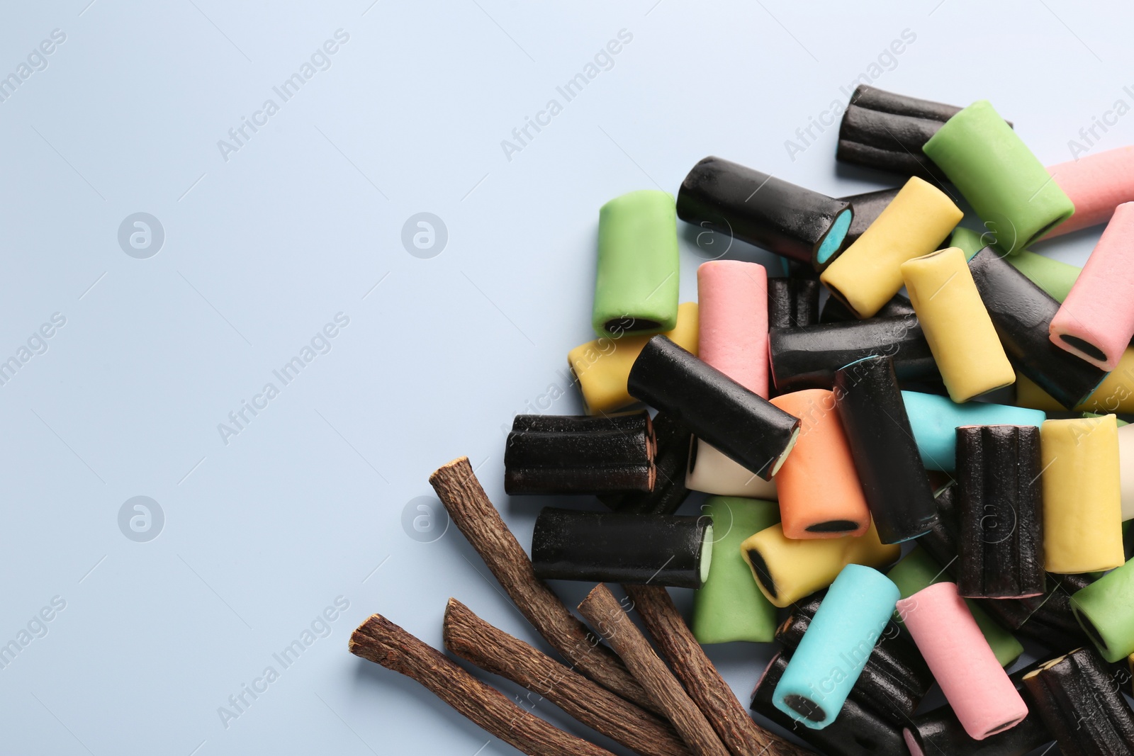 Photo of Tasty candies and dried cut liquorice root on light blue background, flat lay. Space for text