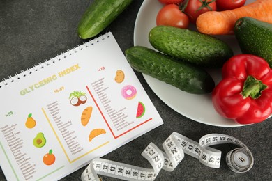 Notebook with information about glycemic index, measuring tape and vegetables on grey table, flat lay